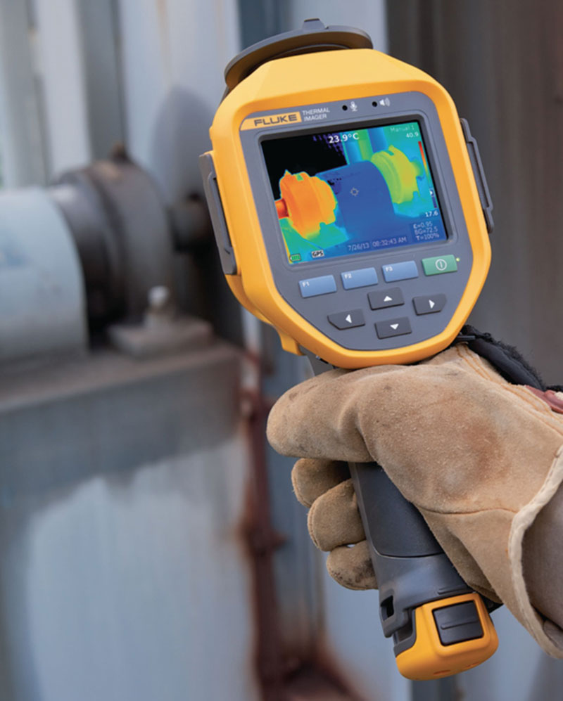 Fluke TI300 thermal imager being held by a gloved hand, aimed at a valve